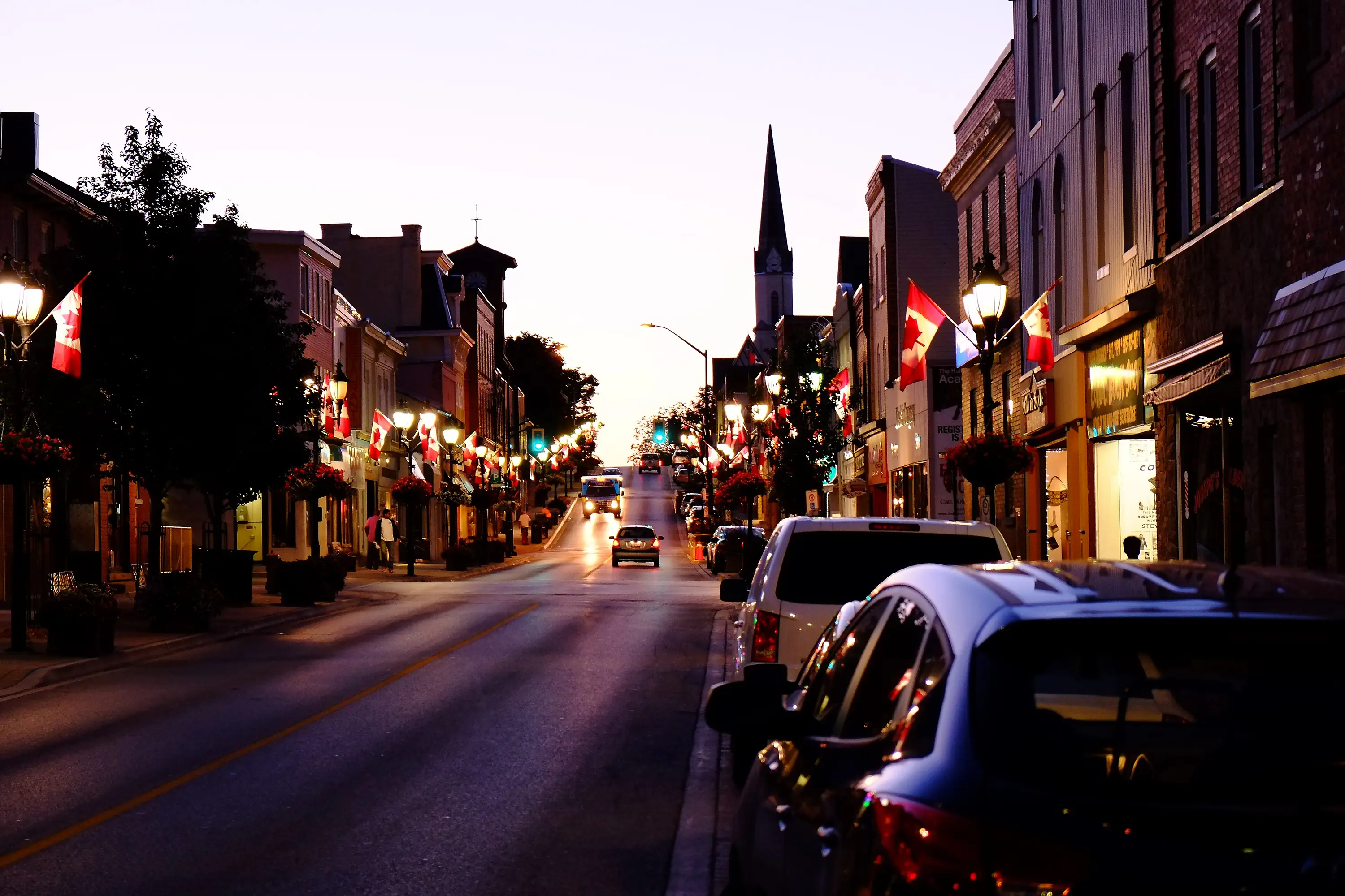 Main Street in downtown Newmarket at dusk, lit storefronts and Canadian flags